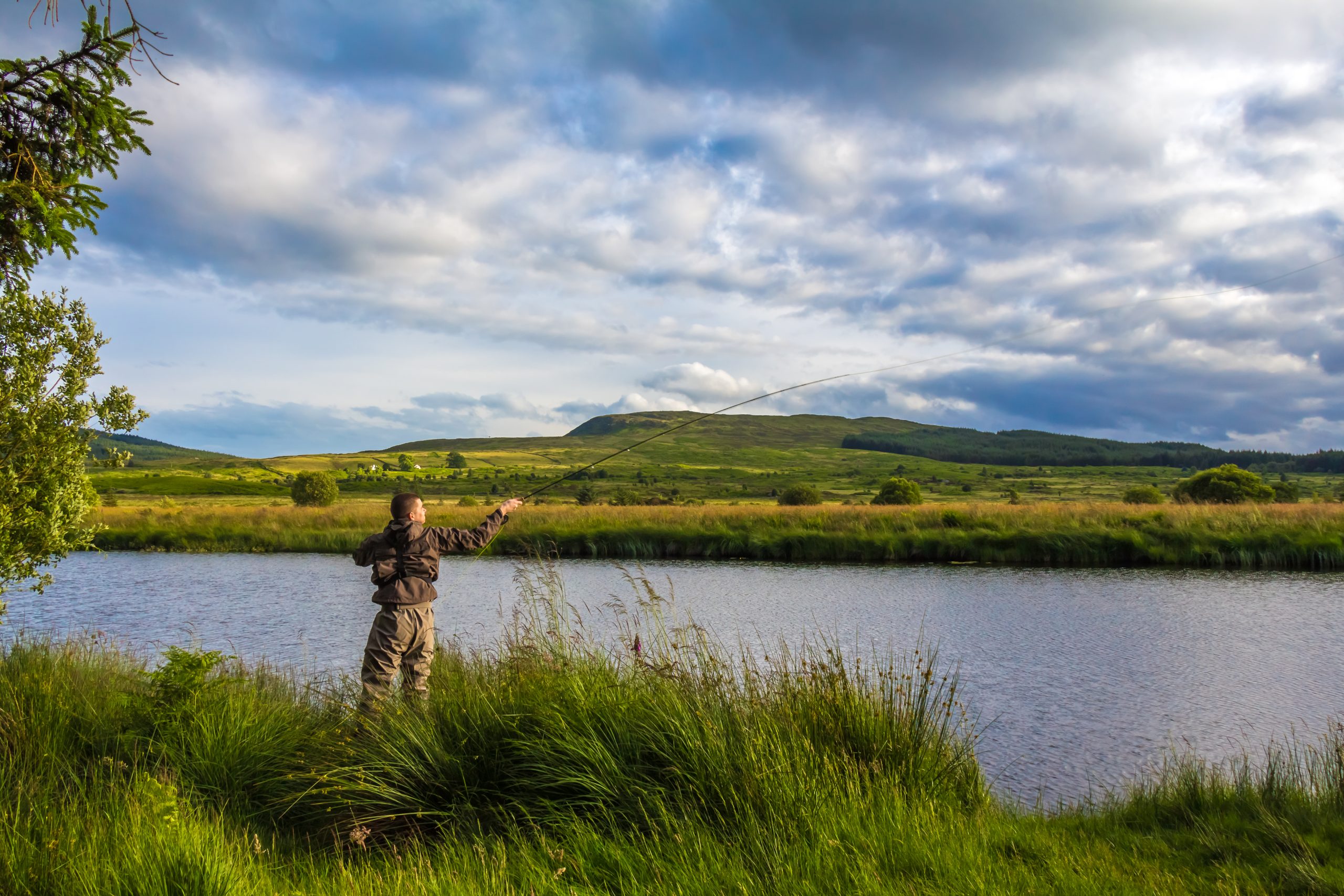 A fisherman fly fishing in the evening sun on the Blackwater of Dee, Galloway, Scotland